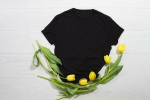 Black t-shirt mockup. Template blank shirt top view. White wooden background. Mother women day holiday. Yellow tulips. Woman tshirt with birthday bouquet flowers. Spring look. Female accessories photo