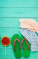 chanclas, caramelo de sandía y toalla. accesorios de playa de verano y espacio de copia sobre fondo de madera azul. vista superior foto