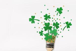 Creative St. Patricks Day concept. Paint brush with green glitter shamrocks and confetti. Minimal St. Patricks Day background photo