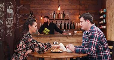 Zoom in shot of beautiful couple drinking coffee in vintage rustic coffee shop pub restaurant. There is a bearded hipster barista in the background at the counter video