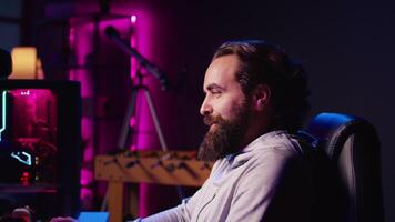 Man in RGB lit studio streaming multiplayer game, chatting with audience while defeating enemies, zoom out shot. Pro gamer using professional equipment to broadcast videogame gameplay to fans video