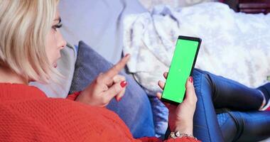 Back view of caucasian woman using phone for christmas shopping laying on sofa. Green screen phone. video