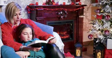 Aan Kerstmis dag terwijl wachtend voor de kerstman moeder is lezing een verhaal naar haar dochter van een boek. video