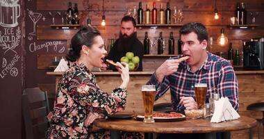 Pizza y cerveza es un valores imágenes presentación un hermosa Pareja en elegante pub o restaurante comiendo Pizza y Bebiendo cerveza. allí es un barbado hipster barman quien sitts a el mostrador en el antecedentes video