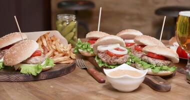 glad parallax schot van breed selectie van hamburgers Aan een houten ronde tafel. in een restaurant, een tafel met snel voedsel bereid voor een groot lunch. video