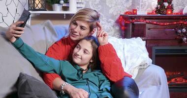 Happy mother and daughter making selfie on christmas day lying on sofa. video