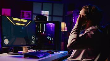glücklich Mann Putten auf Kopfhörer zu kommunizieren mit Teamkollegen online von seine dunkel Leben Zimmer, spielen einnehmend Video Spiele auf Spielen pc beim Computer Schreibtisch, chillen nach Arbeit