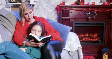 poco ragazza su Natale giorno godendo un' storia a partire dal un' libro con sua madre e lampeggiante luci. video