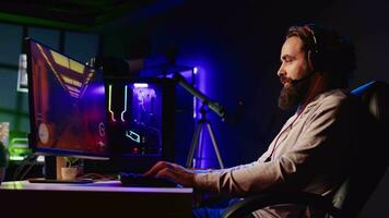 Pro gamer competing in intense online multiplayer videogame with his friends, shooting enemies from living room with rgb lights. Man using gaming computer and headphones for immersive experience video