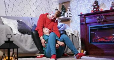 Cheerful parent tickles her little daughter on christmas day sitting next to fireplace wainting for santa. video