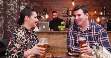 zoom uit schot van Kaukasisch paar drinken bier en aan het eten pizza in wijnoogst rustiek kroeg of restaurant. ze zijn hebben een Super goed tijd, ze praten en lach video