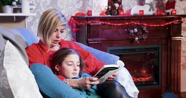 en Navidad día joven de la madre leyendo un historia desde un libro a su pequeño hija. video