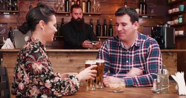 zoom uit schot van gelukkig verliefd paar drinken bier in elegant wijnoogst kroeg restaurant. ze zijn hebben een veel van plezier. een barista is werken in de achtergrond Bij de balie. video