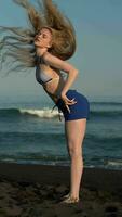 joven rubia mujer voltear espalda largo cabello. sensualidad hembra en a rayas bikini parte superior y azul pantalones cortos video