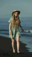 Sensual female in summer dress, straw hat and barefoot walking on black sands of Pacific Ocean beach video