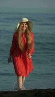 souriant femme en marchant sur noir sables plage de océan. de face vue de pieds nus femelle dans été robe video