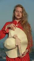 Woman putting on straw sun hat and straightens long hair. Model in summer red polka dots dress video