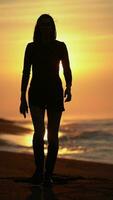 Woman in short dress walking on sandy beach at sunrise on background solar disk rising above horizon video