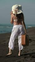 Rear view of unrecognizable female holding suitcase standing on sandy beach during summer holidays video