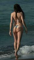 posterior ver irreconocible maduro adulto hembra en bikini caminando en playa entra agua rotura olas video