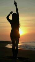 posteriore Visualizza silhouette donna con mani sollevato in piedi sabbioso spiaggia a Alba. lento movimento, verticale video