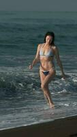 lleno longitud mujer en bikini corriendo negro arenoso playa tobillo profundo en agua de olas de Pacífico Oceano video
