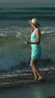 Barefoot female in breaking waves, splashes on sandy beach. Full length woman during beach holidays video