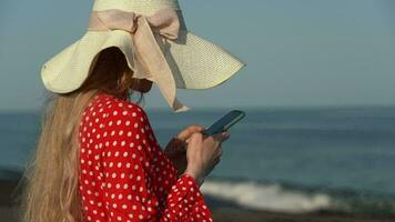 Young woman using smartphone on beach, holding phone in hands, touch screen and text messaging video
