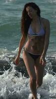 sensual Delgado mujer en bikini caminando en playa tobillo profundo en agua de rotura olas de Pacífico Oceano video