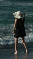 Barefoot woman standing on beach, kicking and raising splashes breaking waves crashing on seashore video