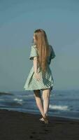 Rear view woman walking along beach, then turning around and poses playfully looking at camera video