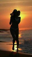 Silhouette of woman in bikini on sandy beach at sunrise on background of solar disk rising horizon video