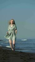 Smiling woman in summer polka dot dress and barefoot running on black sands beach of Pacific Ocean video