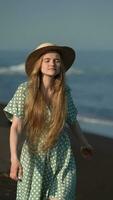 Smiling sensual blonde female in straw hat, summer polka dot dress walking on beach of Pacific Ocean video