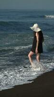 Unrecognizable woman with long legs on beach kicking and raising splashes in waves crashing seashore video