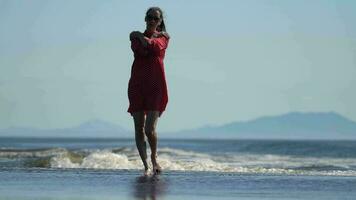 Sensuality woman walking on beach of Pacific Ocean, wearing red summer babydoll polka dot dress video