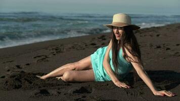 50 jaar oud sensualiteit slank vrouw met lang poten zittend Aan zomer strand met zwart zand video