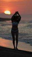 descalzo mujer en bikini, Paja Dom sombrero camina en playa a amanecer. hembra disfrute a dorado hora video