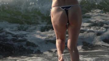 Closeup back view of slim woman in bikini bottom moving in splashing breaking wave. Slow motion video