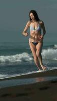 mujer en bikini corriendo en negro arenoso playa de Pacífico oceánica en antecedentes de rotura olas video