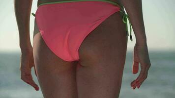 detailopname visie van vrouw lichaam in roze bikini bodem draaien, langzaam in beweging haar taille, heupen en billen video