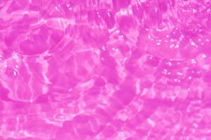 Purple water splashes on the surface ripple blur. Defocus blurred transparent pink colored clear calm water surface texture with splash and bubble. Water waves with shining pattern texture background. photo