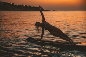 Woman Doing SUP Balance Yoga on Sunset photo