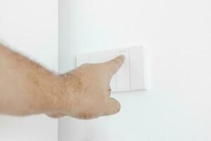 Man uses his finger to turn on a light switch on white wall. Plug studio apartment power supply. Light switch. Power outlet. Concept of technology, connection, power saving, energy saving. photo