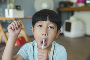 Close up portrait of Asian boy with black bangs, black eyes with a smiling face wearing a light green shirt look at camera and sitting on the floor of his house and hand holding pencil to draw. photo