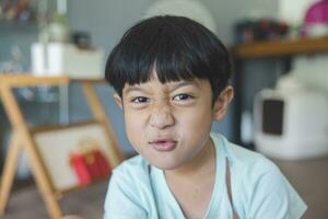 Close up portrait of Asian boy with black bangs, black eyes with a smiling face wearing a light green shirt look at camera and sitting on the floor of his house and hand holding pencil to draw. photo