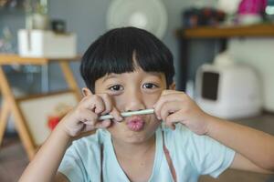 Close up portrait of Asian boy with black bangs, black eyes with a smiling face wearing a light green shirt look at camera and sitting on the floor of his house and hand holding pencil to draw. photo