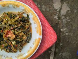 Stir-fried spicy kale with strong spices mixed with cempoka and tepus flowers served on a plate photo