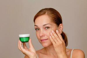 Portrait of caucasian middle aged woman face with freckles showing soft skin by fingers holding cream photo