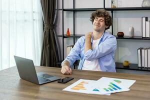 Caucasian man is working at his home office while having scapula and shoulder pain, back pain from office syndrome photo